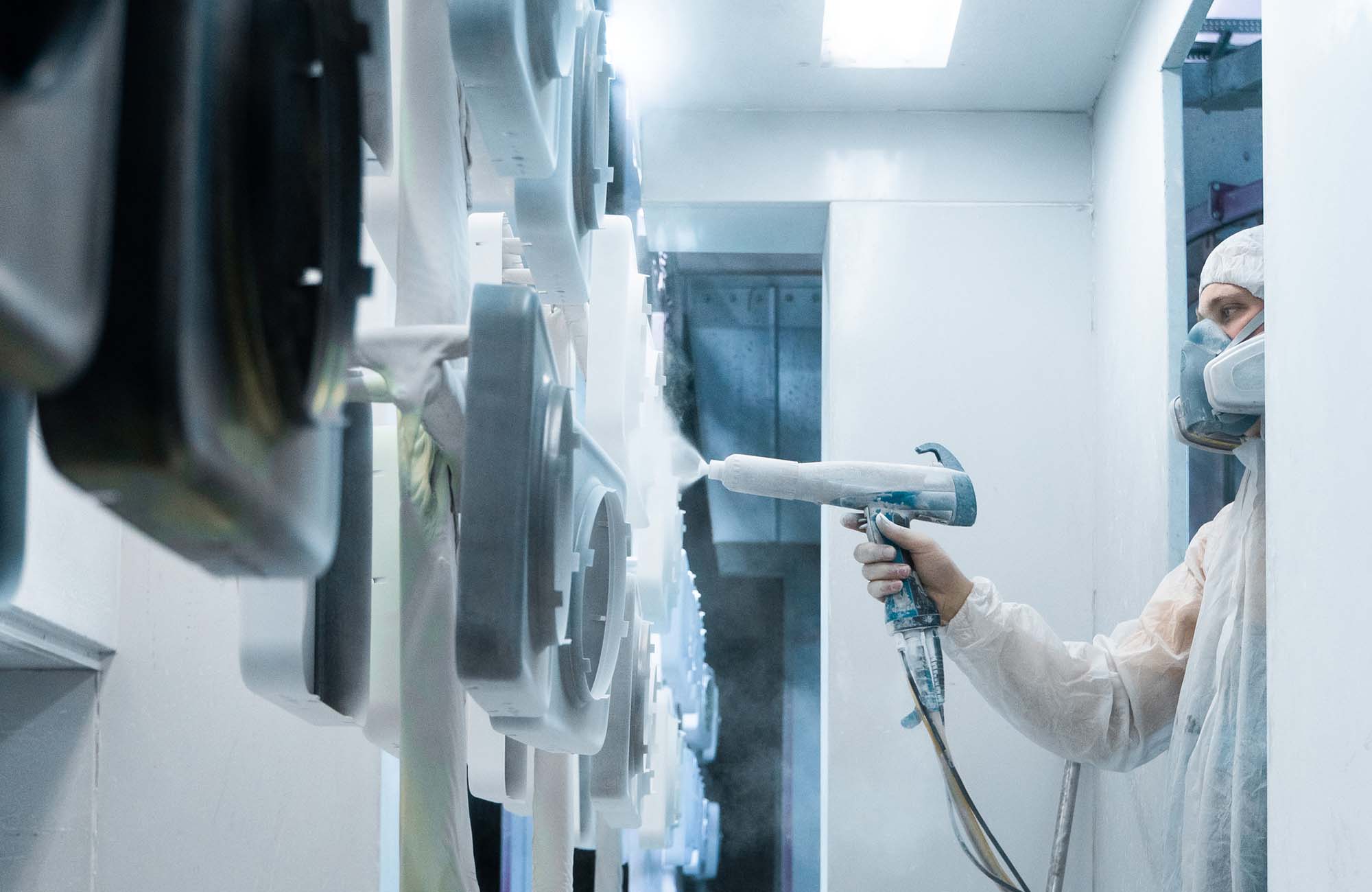 Powder coating of metal parts. Man in a protective suit sprays white powder paint from a gun on metal products.